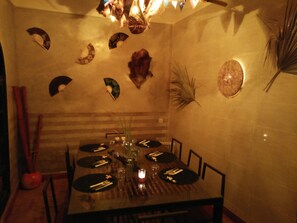 A dining area with a round table set for six, surrounded by chairs. Decorative wall art and a small plant are visible. - Riad Nomades (Marrakech)