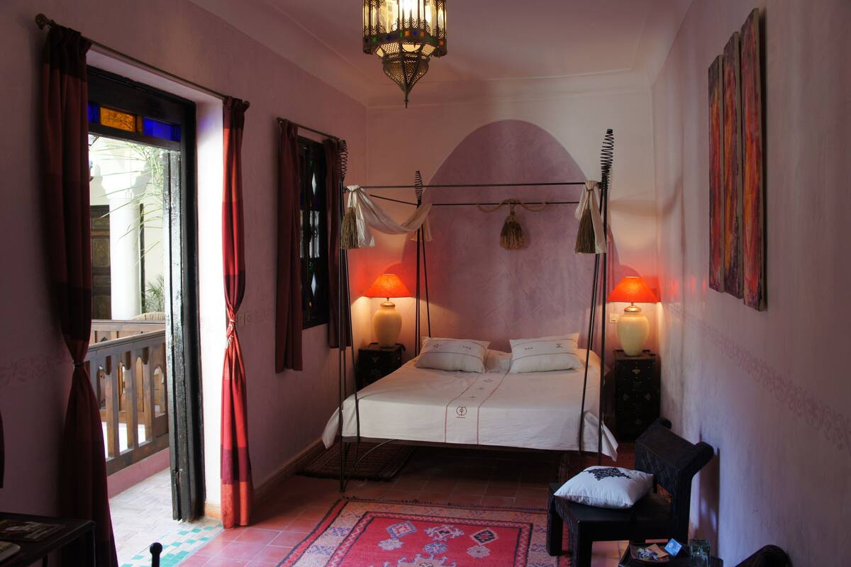 A bedroom with a four-poster bed, two bedside lamps, a chair, and a decorative rug.