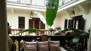 A cozy seating area with a cushioned bench and pillows, surrounded by large green plants and traditional lanterns. - Riad Nomades (Marrakech)