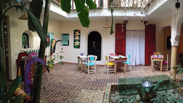 A spacious indoor area with a tiled floor, multiple tables and chairs, and a central decorative water feature. - Riad Nomades (Marrakech)