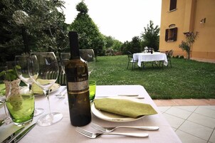 Un montaje para comer al aire libre con una mesa preparada para dos personas, que incluye una botella de vino, copas y cubiertos.