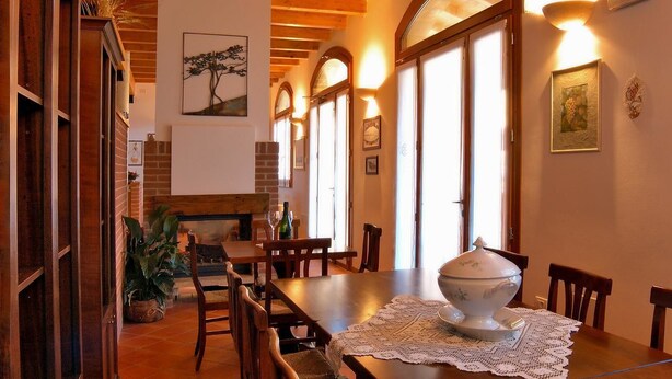 A dining area with wooden furniture, a fireplace, and large windows with arched tops. - Agriturismo Borgo delle Vigne (Zola Predosa)