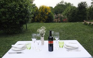 Mesa lista al aire libre con una botella de vino, copas y cubiertos.