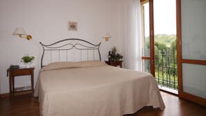 A bedroom with a bed, two bedside tables, a nightstand, a window with a view, and a ceiling with wooden beams. - Agriturismo Borgo delle Vigne (Zola Predosa)