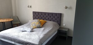 A neatly made bed with a grey headboard, a patterned pillow, and a small bedside table. - Résidence Tournet (Kraków)