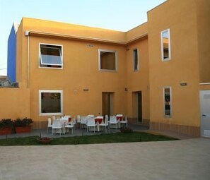 A building with a yellow facade, multiple windows, and a courtyard with white tables and chairs. - Hotel San Martino (Syracuse)
