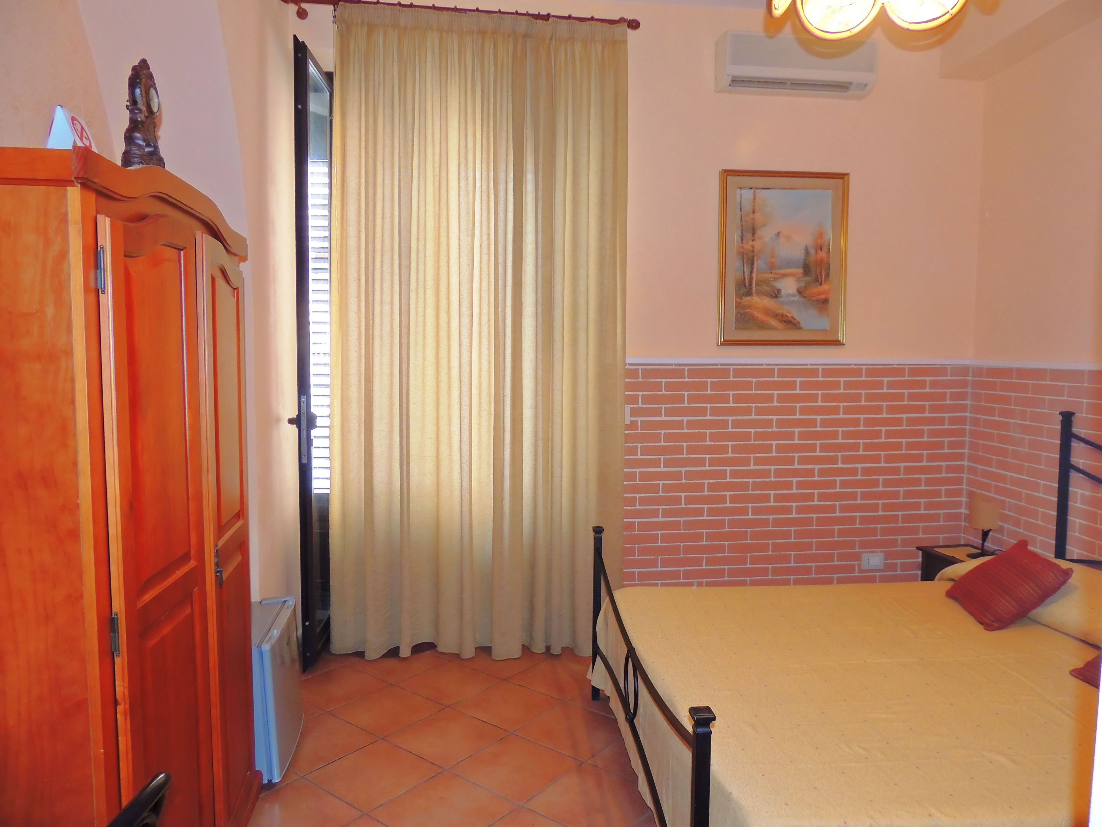 Ein Schlafzimmer mit Bett, Kleiderschrank, Vorhang, Gemälde und einer Ziegelwand.
