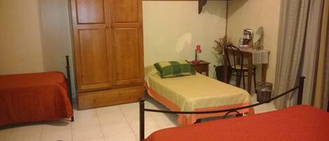 A room with two single beds, a wooden wardrobe, a desk with a chair, a television, and a small table with a plant.