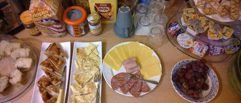 A table with various food items and condiments, including plates of sliced bread, cheese, and meats, as well as jars of preserves and condiments.