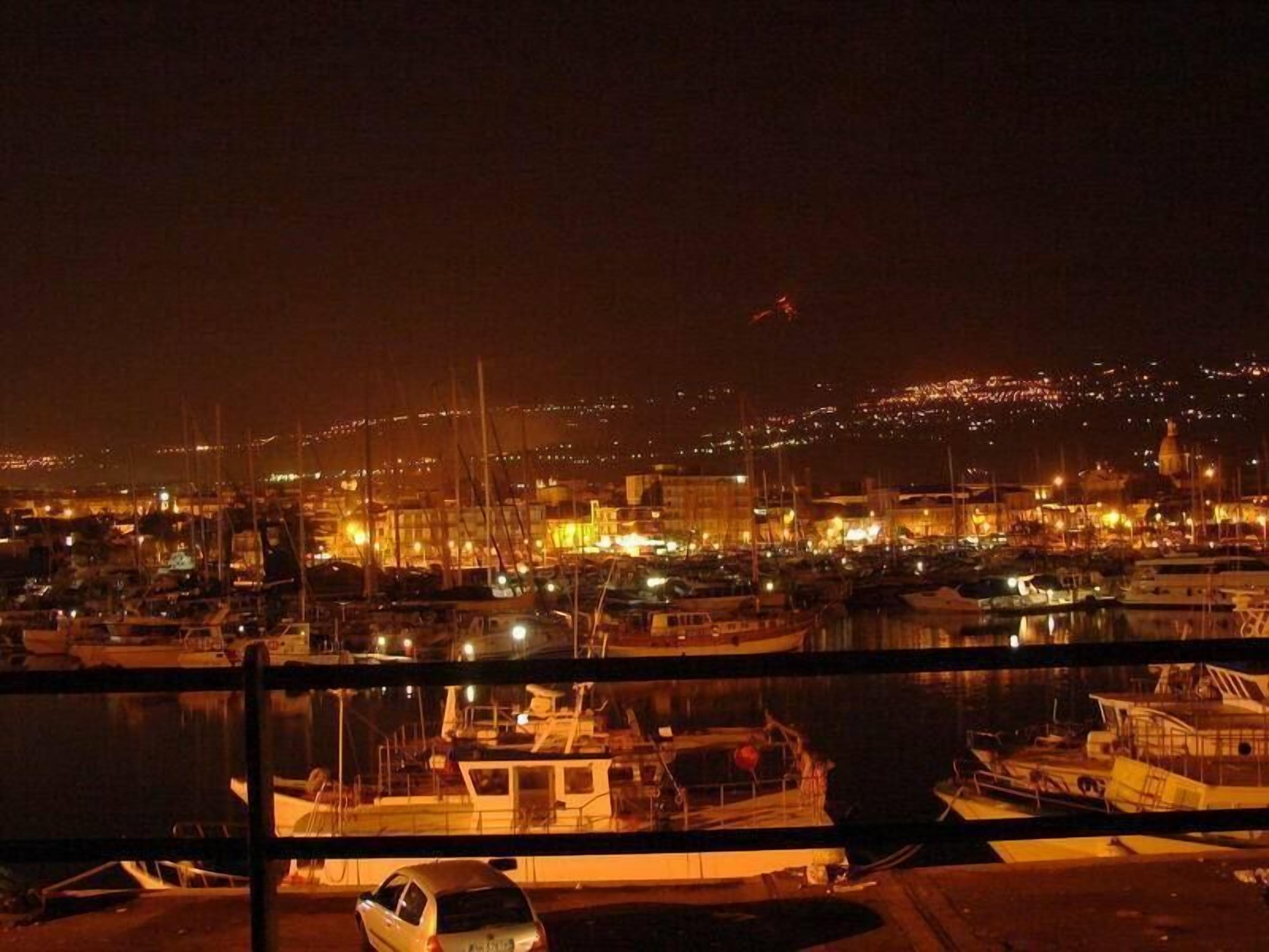 Un port de plaisance illuminé la nuit, avec des bateaux amarrés et les lumières de la ville en arrière-plan.