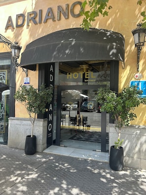 The entrance to Adriano Hotel Boutique with a black awning, potted plants, and a visible interior through the glass doors. - Adriano Hotel Boutique Sevilla (Seville)
