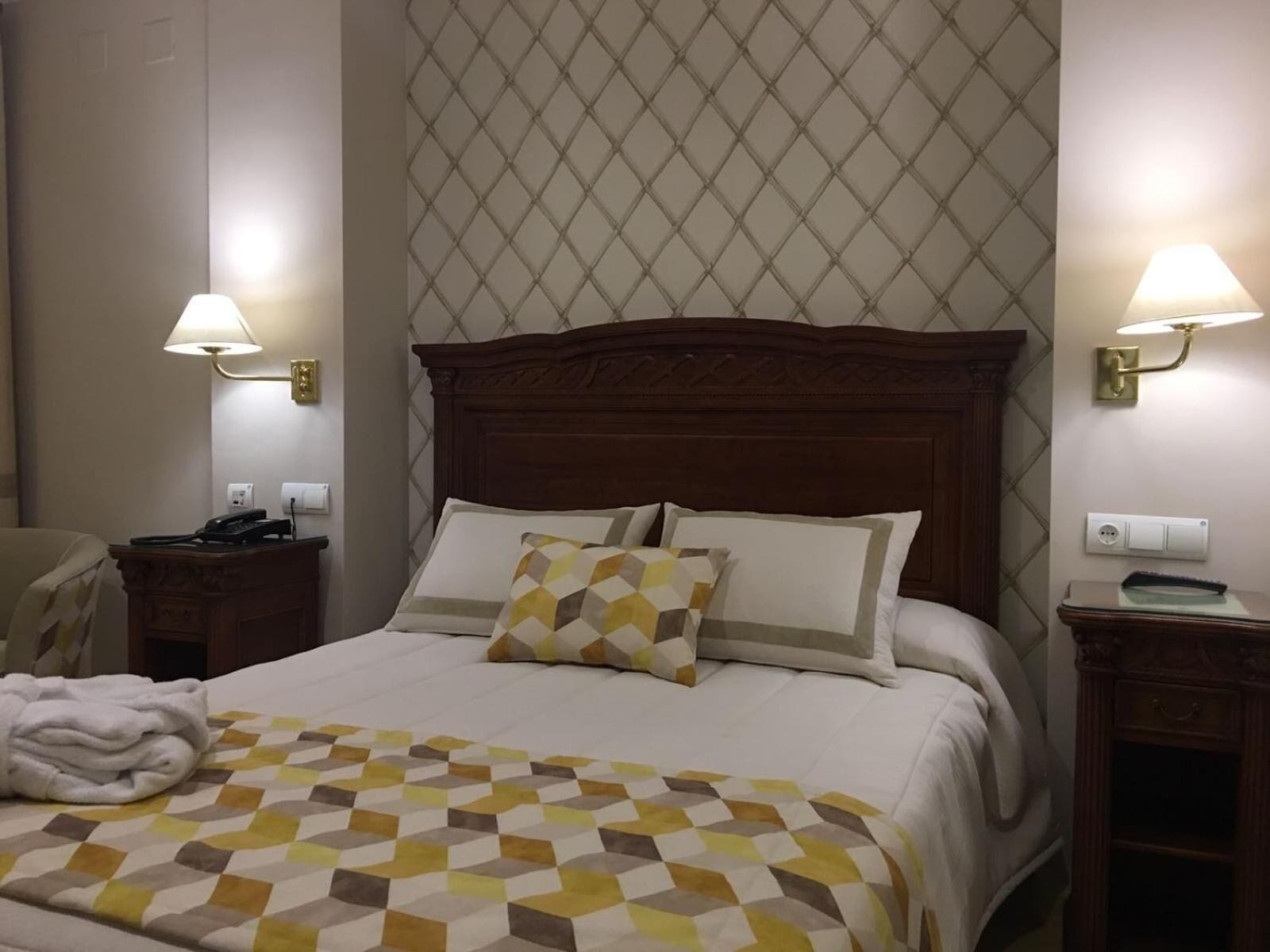A hotel room with a large bed, two bedside tables, a chair, and a robe on the bed.