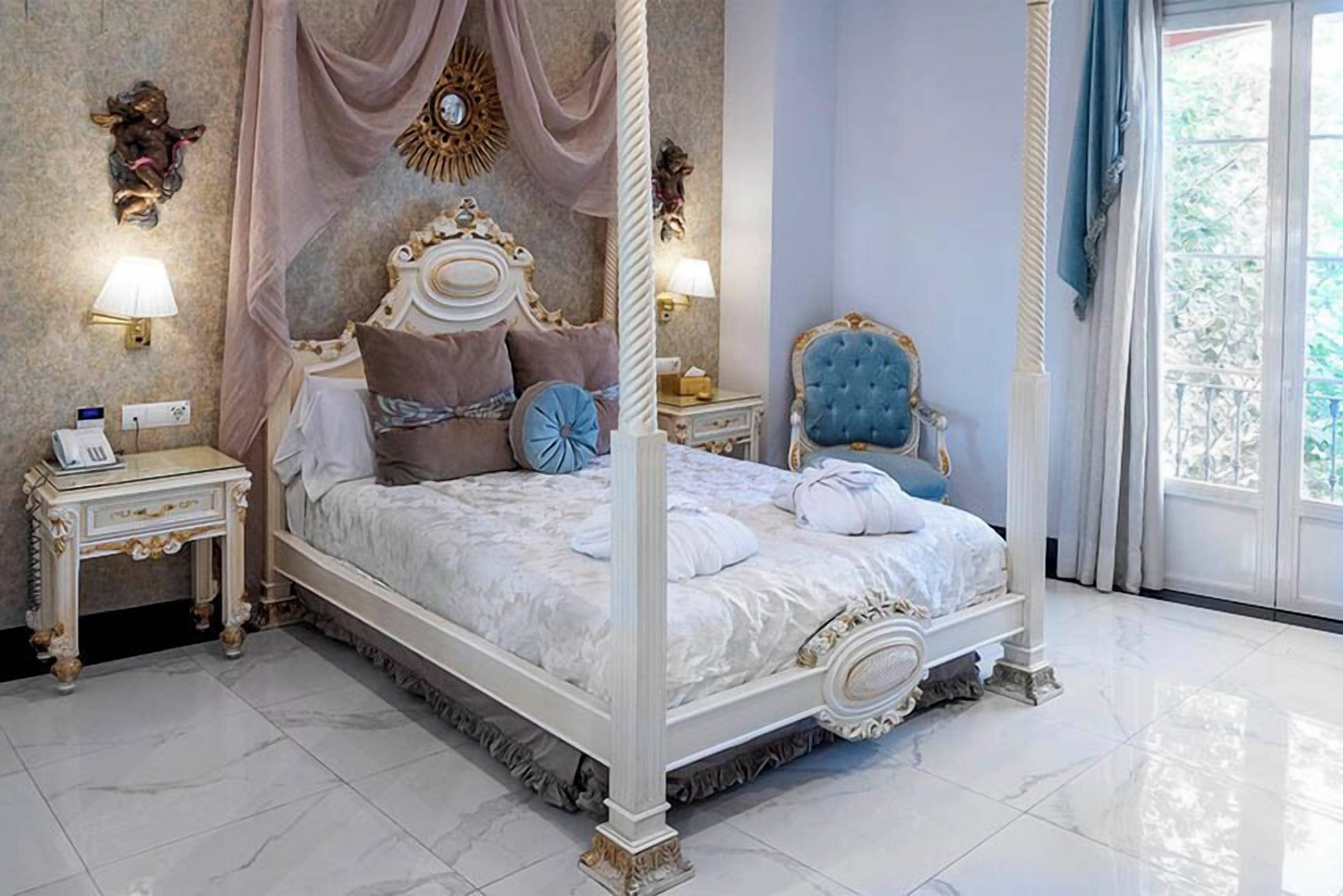 A four-poster bed with a canopy, two bedside tables, a chair, and a view of the outdoors.