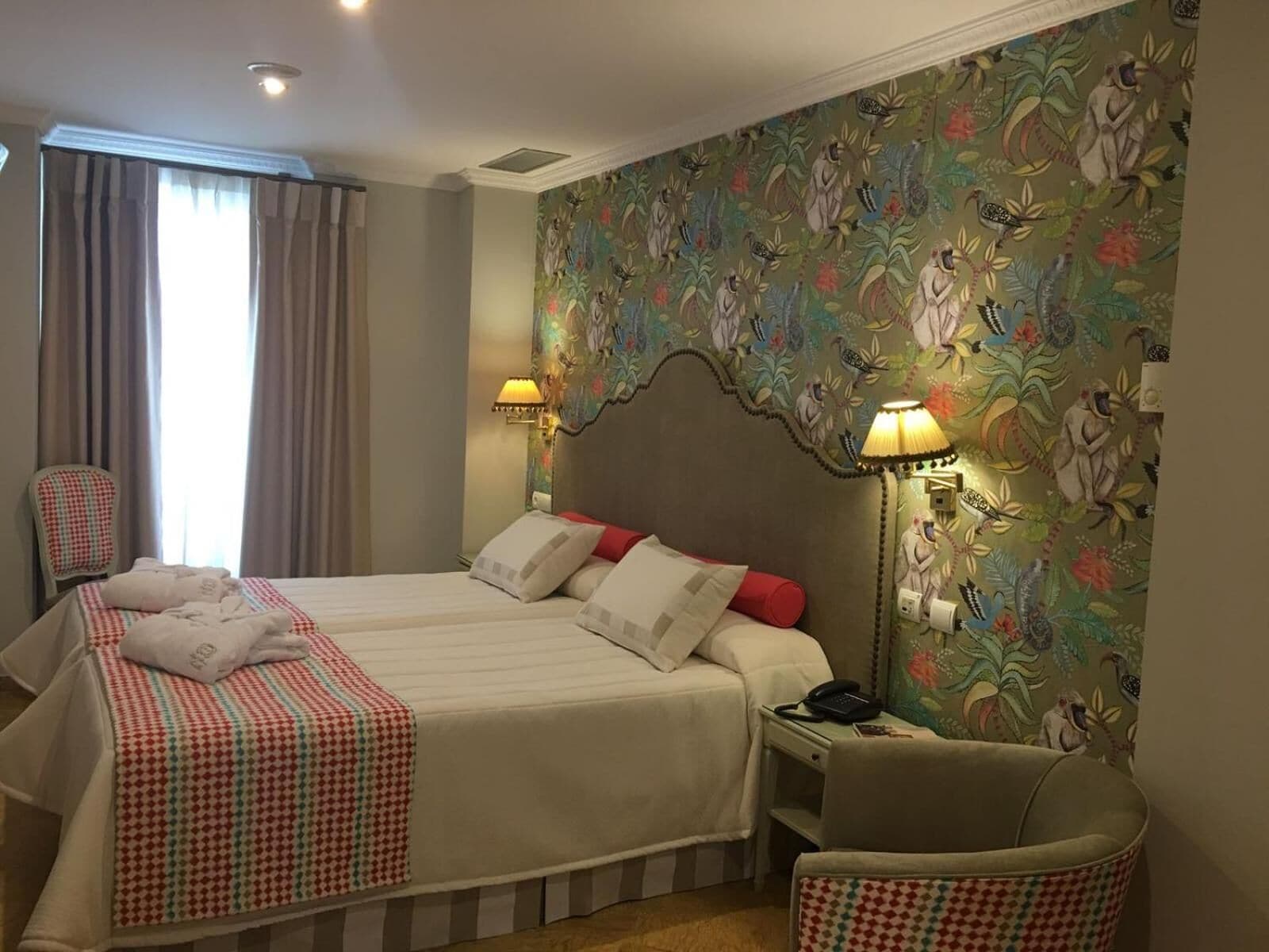 Une chambre d’hôtel avec deux lits, une chaise, un bureau et un mur orné d’un motif floral.