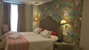 Une chambre d’hôtel avec deux lits, une chaise, un bureau et un mur orné d’un motif floral.