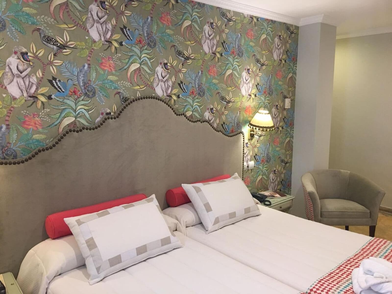 A hotel room with a bed, two pillows, a nightstand, a lamp, and a chair.