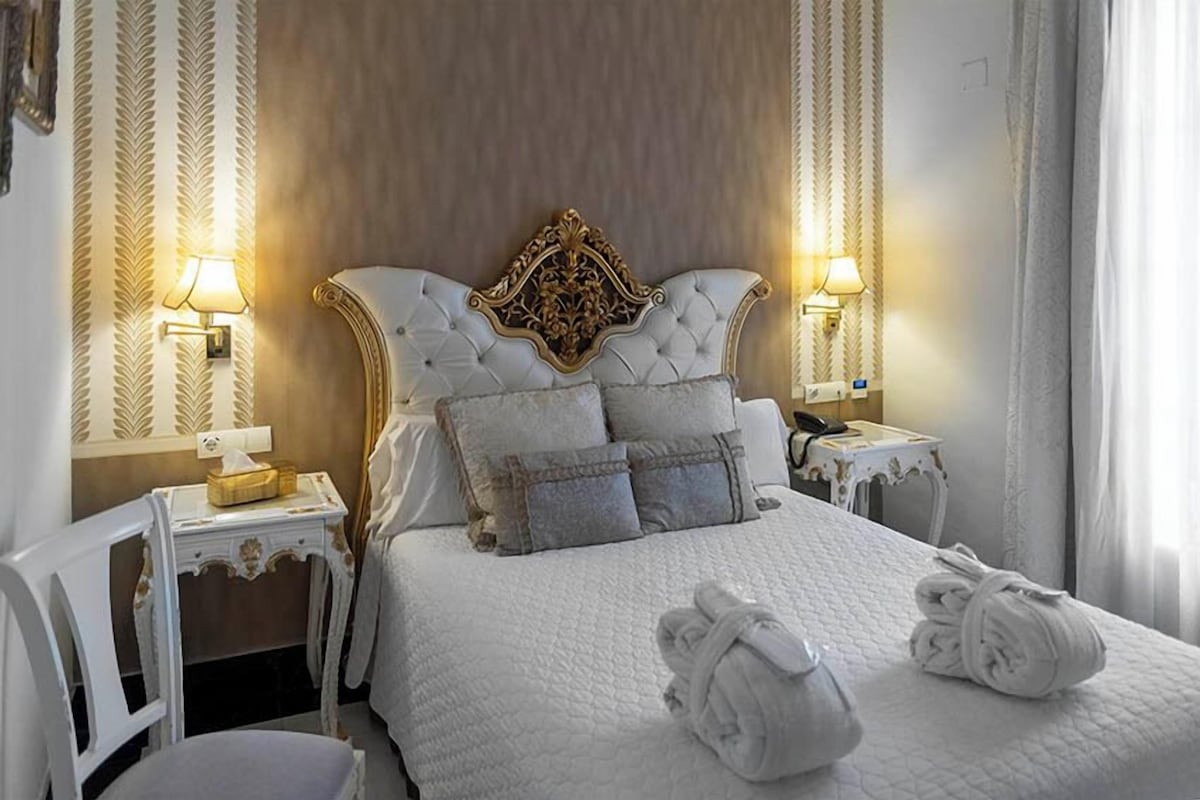 A hotel room with a large bed, two bedside tables, a headboard, and two wall-mounted lamps.