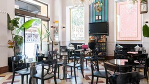 Un restaurante con varias mesas y sillas, un candelabro y grandes ventanales con paneles de vidrio decorativos.
