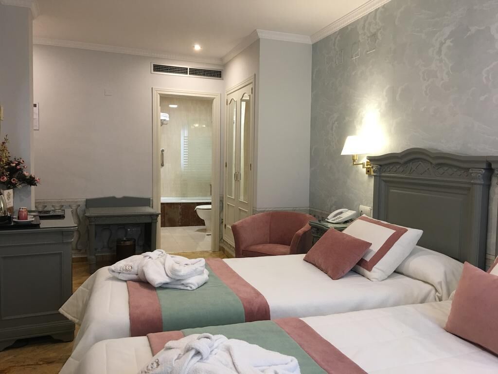 A hotel room with two beds, a desk, a chair, a mirror, and a lamp.