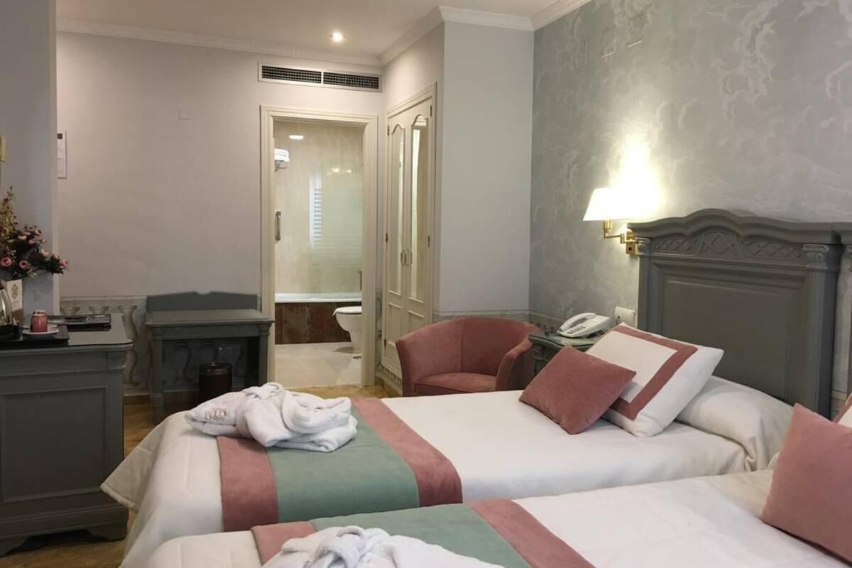 A hotel room with two beds, a desk, a chair, a mirror, and a lamp.