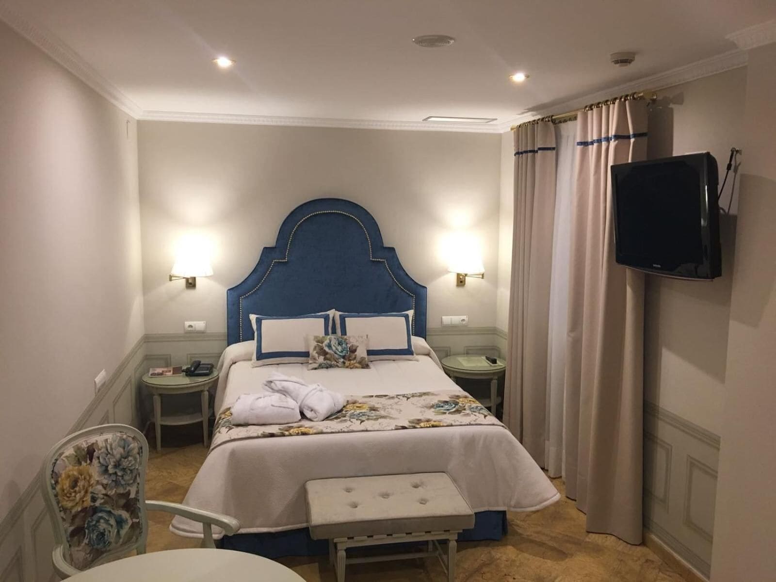 A hotel room with a large bed, two bedside tables, a flat-screen TV, a chair, and a bench.