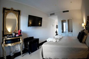 A hotel room with a large bed, a TV mounted on the wall, a vanity with a mirror, and a door leading to another room.