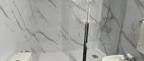 A bathroom with a toilet, bidet, and glass-enclosed shower.