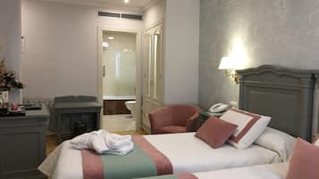 A hotel room with two beds, a desk, a chair, a bathroom, and a lamp.