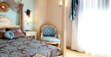 A bedroom with a large bed, a chair, a nightstand, and a wall-mounted light fixture.