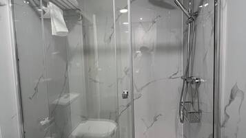 Une cabine de douche fermée par des parois en verre, équipée d’un pommeau de douche à main et d’un flexible de douche.