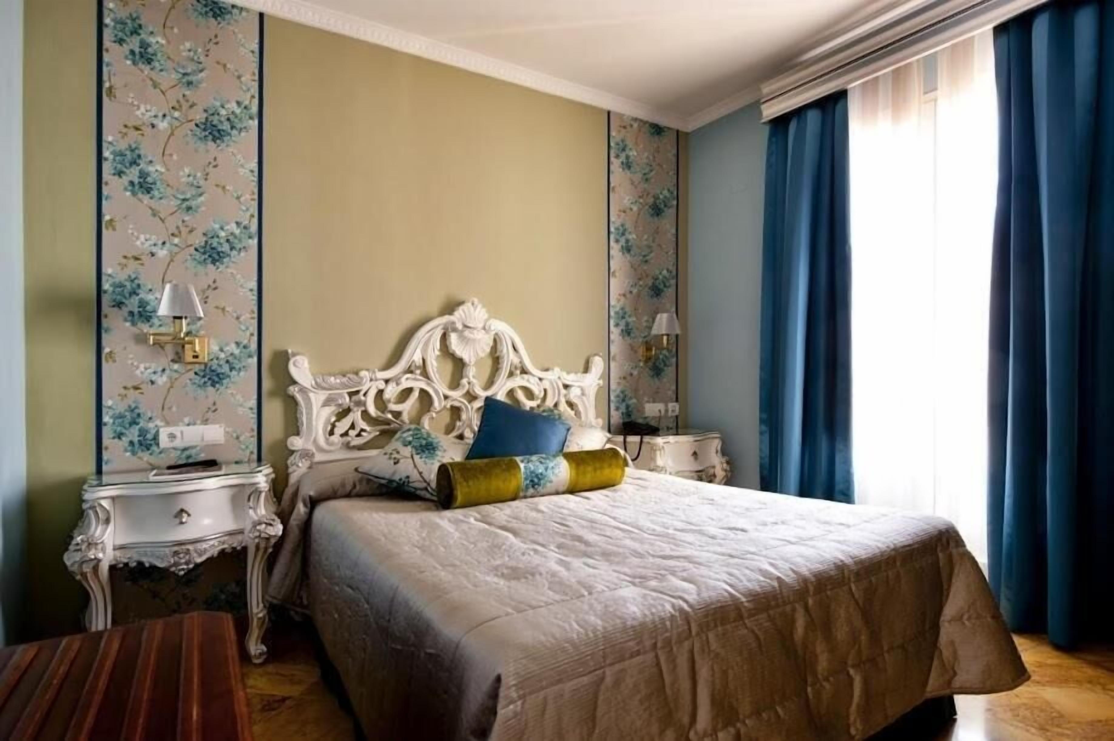 Une chambre avec un grand lit, deux tables de chevet et une fenêtre ornée de rideaux bleus.