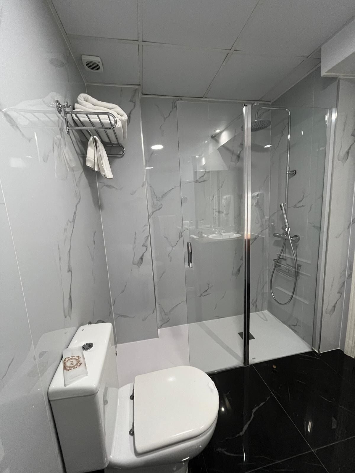 A modern bathroom with a toilet, a glass-enclosed shower, and marble walls.
