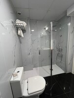 A modern bathroom with a toilet, a glass-enclosed shower, and marble walls.