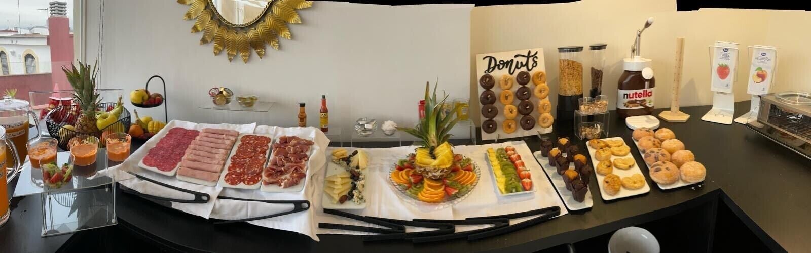 A buffet table with various food items including meats, fruits, pastries, and donuts.