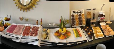 Una mesa de buffet con diversos alimentos, incluyendo carnes, frutas, pasteles y donas.
