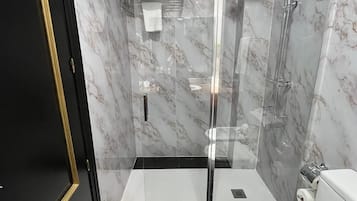 Un baño moderno con ducha de vidrio, inodoro blanco y paredes de mármol.