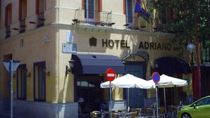 Un hotel con fachada clásica, mesas al aire libre y un cielo azul despejado.