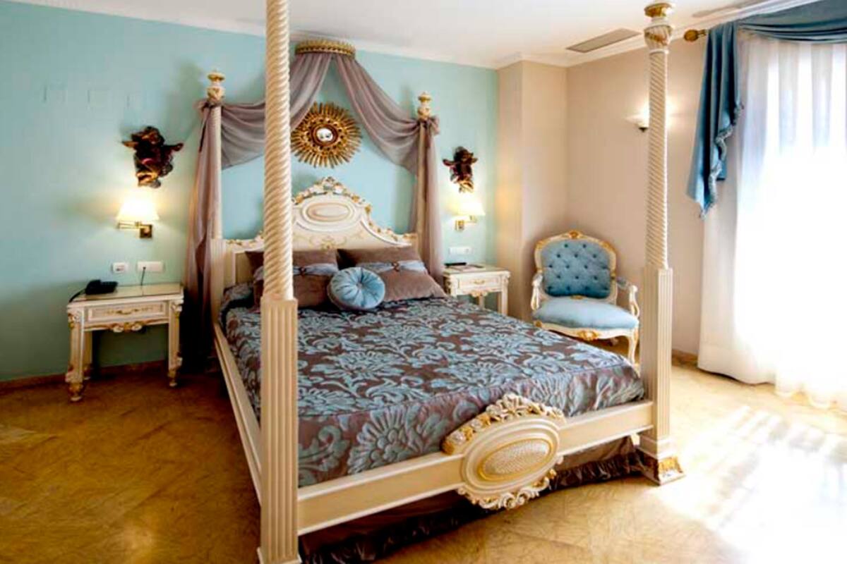 Un lit à baldaquin, une table de chevet, une chaise et une lampe fixée au mur.