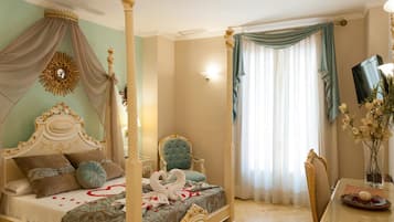 Un lit à baldaquin avec une tête de lit décorée, un fauteuil à capitons, une table à manger ornée d’un vase de fleurs et un téléviseur fixé au mur.
