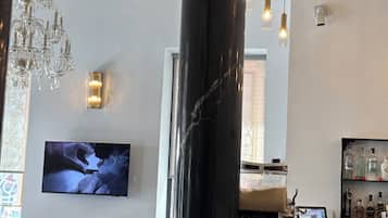 A bar area with a marble column, black chairs, a television, and a bar counter with bottles.
