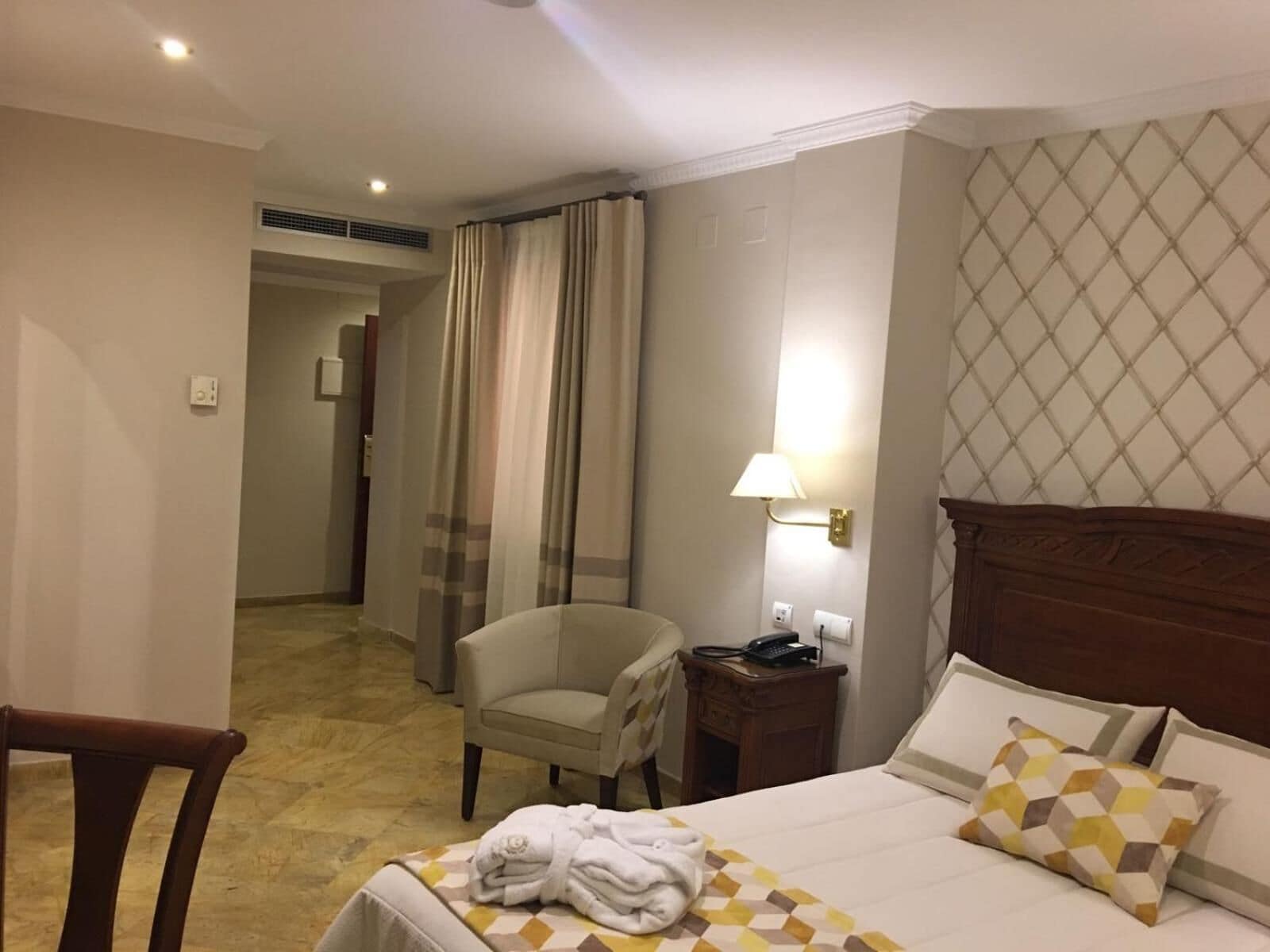 Une chambre d’hôtel avec un lit, une chaise, une table de chevet et une lampe.