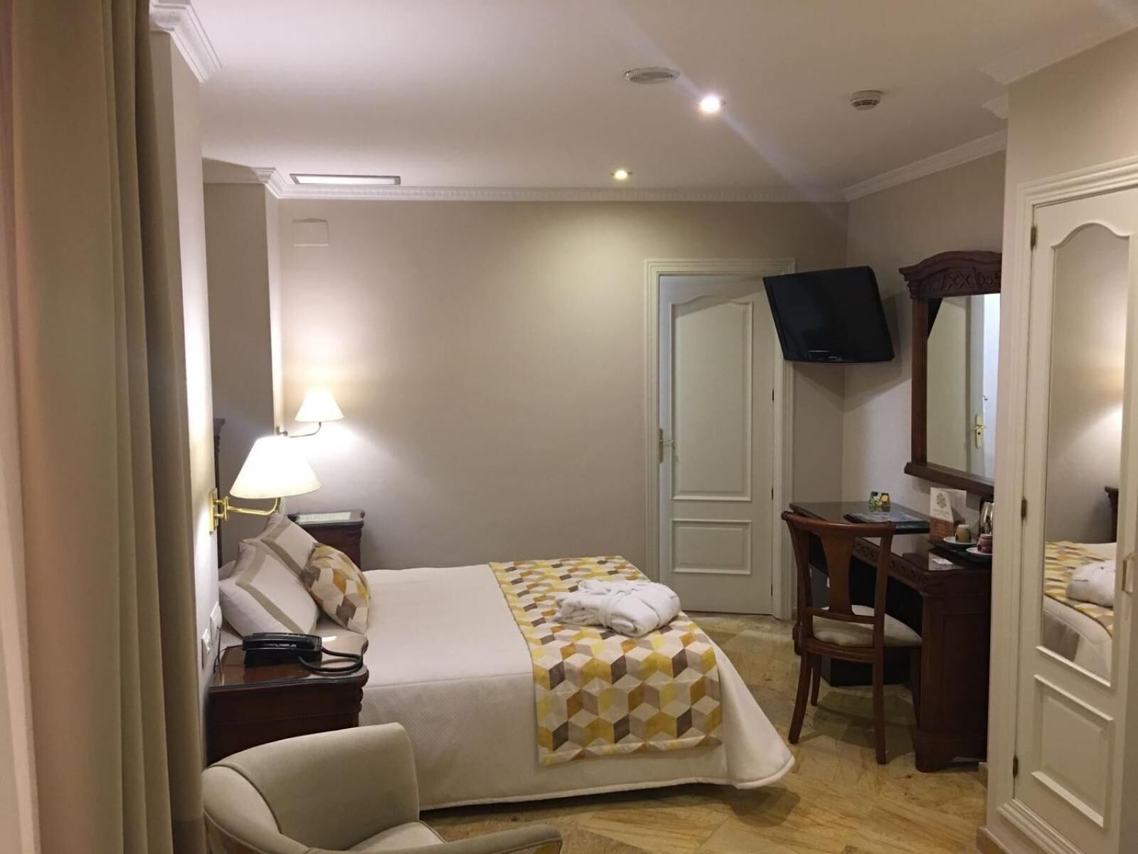 Una habitación de hotel con cama, escritorio, silla, televisor y armario.