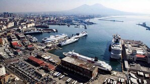 Un paysage urbain côtier avec un port de plaisance, où l’on aperçoit de grands navires de croisière amarrés, et une montagne imposante en arrière-plan.