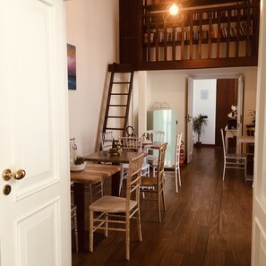 A dining area with a wooden table and chairs, a ladder, and a bookshelf in the background. - Hotiday Napoli Colors (Naples)
