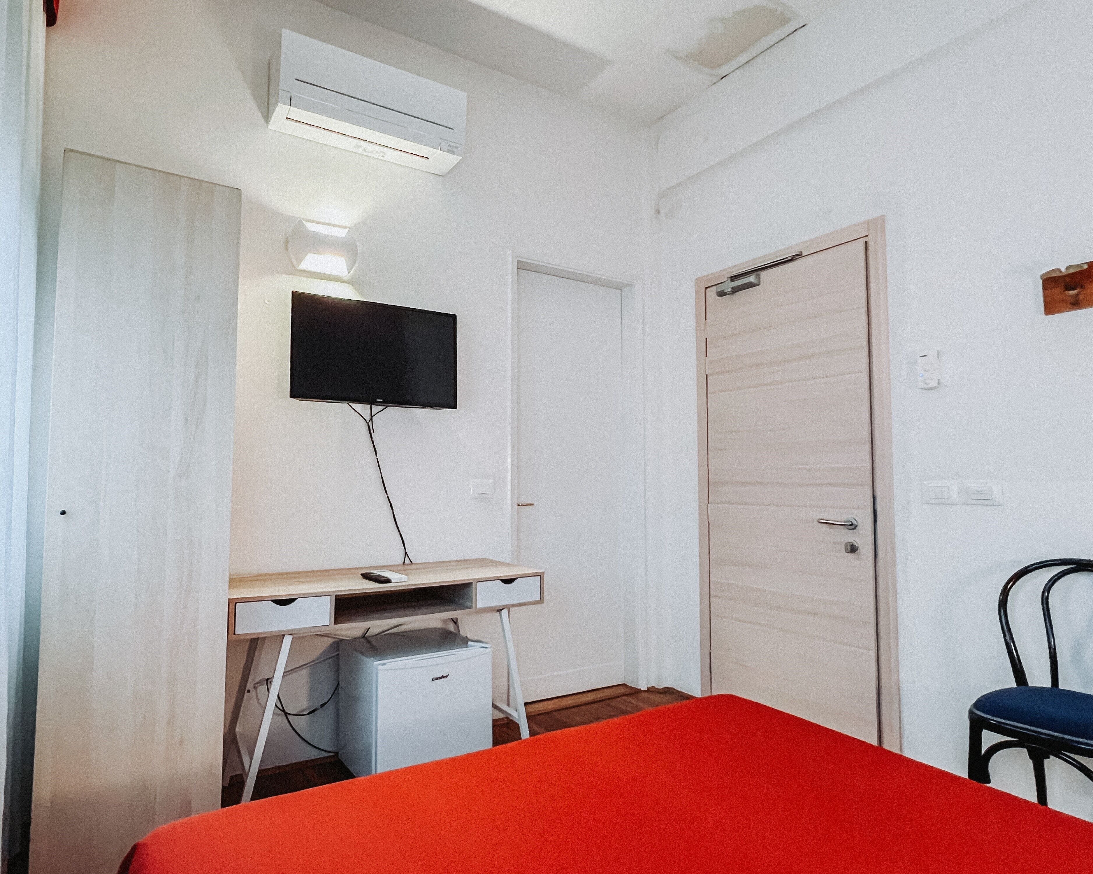 Un dormitorio con cama, escritorio, televisor, aire acondicionado y armario.