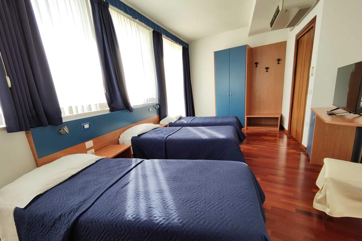 A hotel room with two beds, a wooden desk, a television, and a wardrobe.