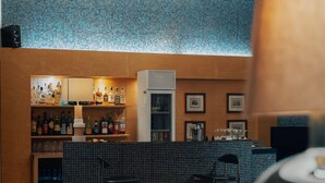 Zona de bar con estantes de botellas de licor y vasos, un refrigerador y cuadros en la pared.