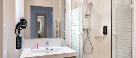 A modern bathroom with a white sink, mirror, and glass shower enclosure.