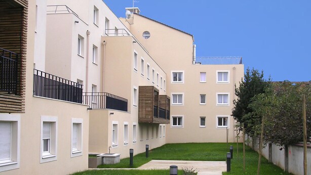 Een modern appartementencomplex met meerdere balkons, een centrale binnentuin en een verzorgd gazon.