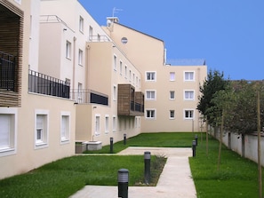 Ein modernes Apartmenthaus mit mehreren Balkonen, einem Innenhof und einem gepflegten Rasen.